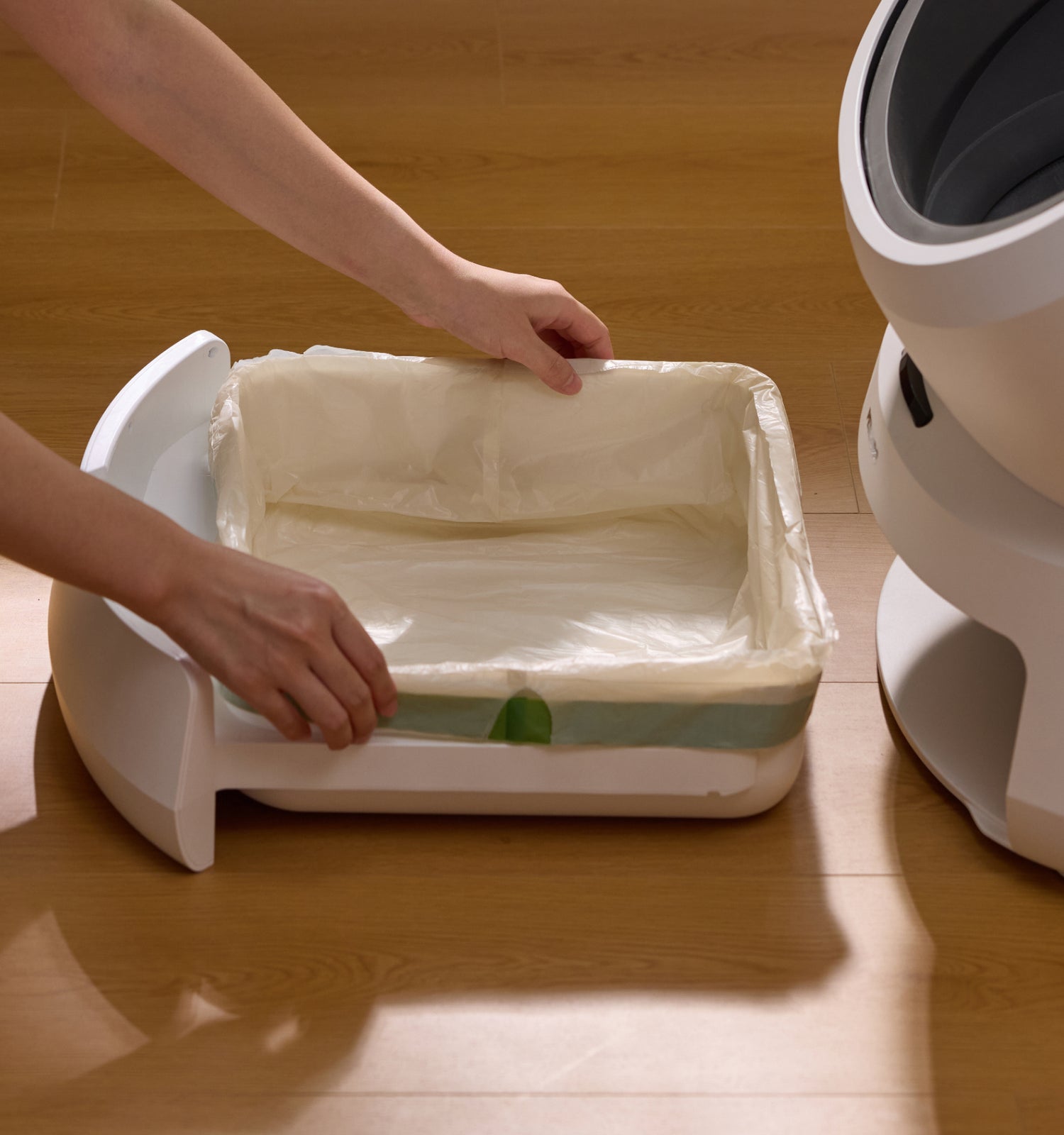 Petlibro PETLIBRO cat pet litter box tray with liner being inserted on wood floor near fountain and automatic feeder